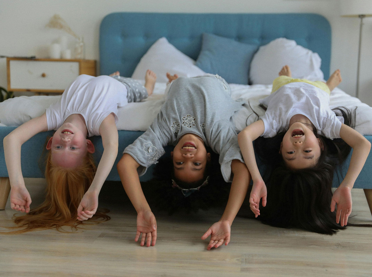 3 happy girls hang upside down off a bed edge
