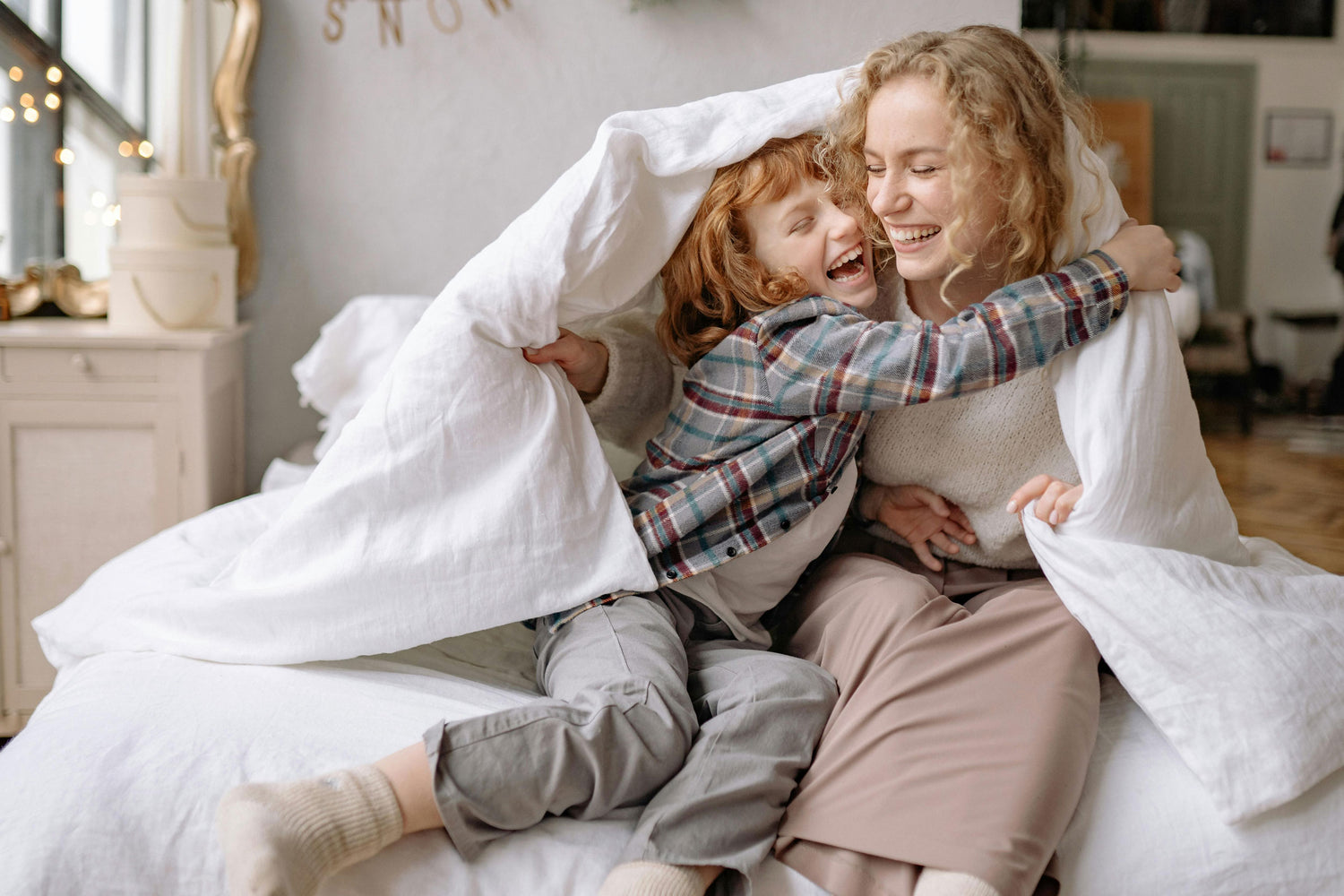 Laughing mother and son on a bed with a blanket 