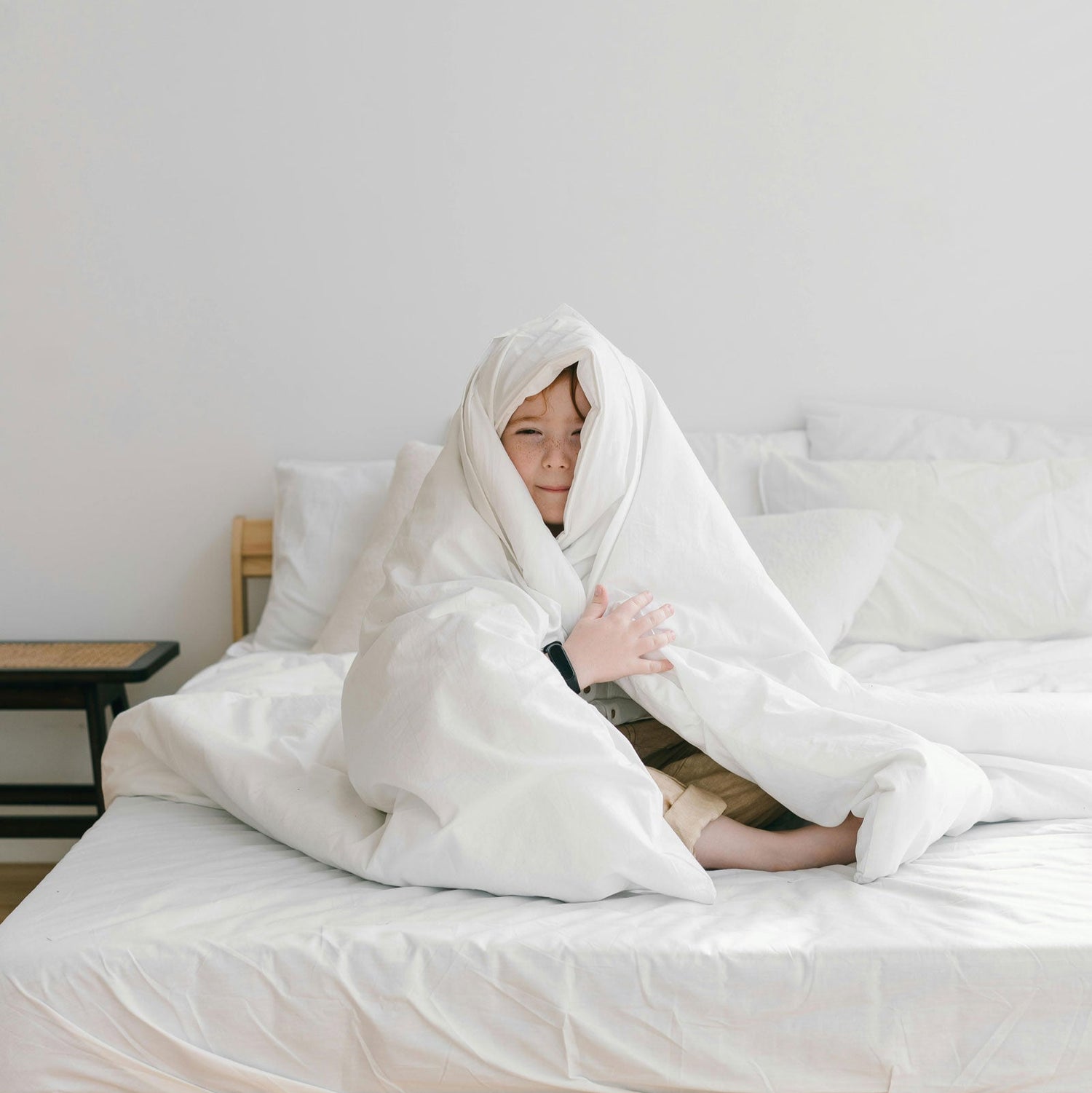 Happy young boy sitting on bed wrapped in blanket