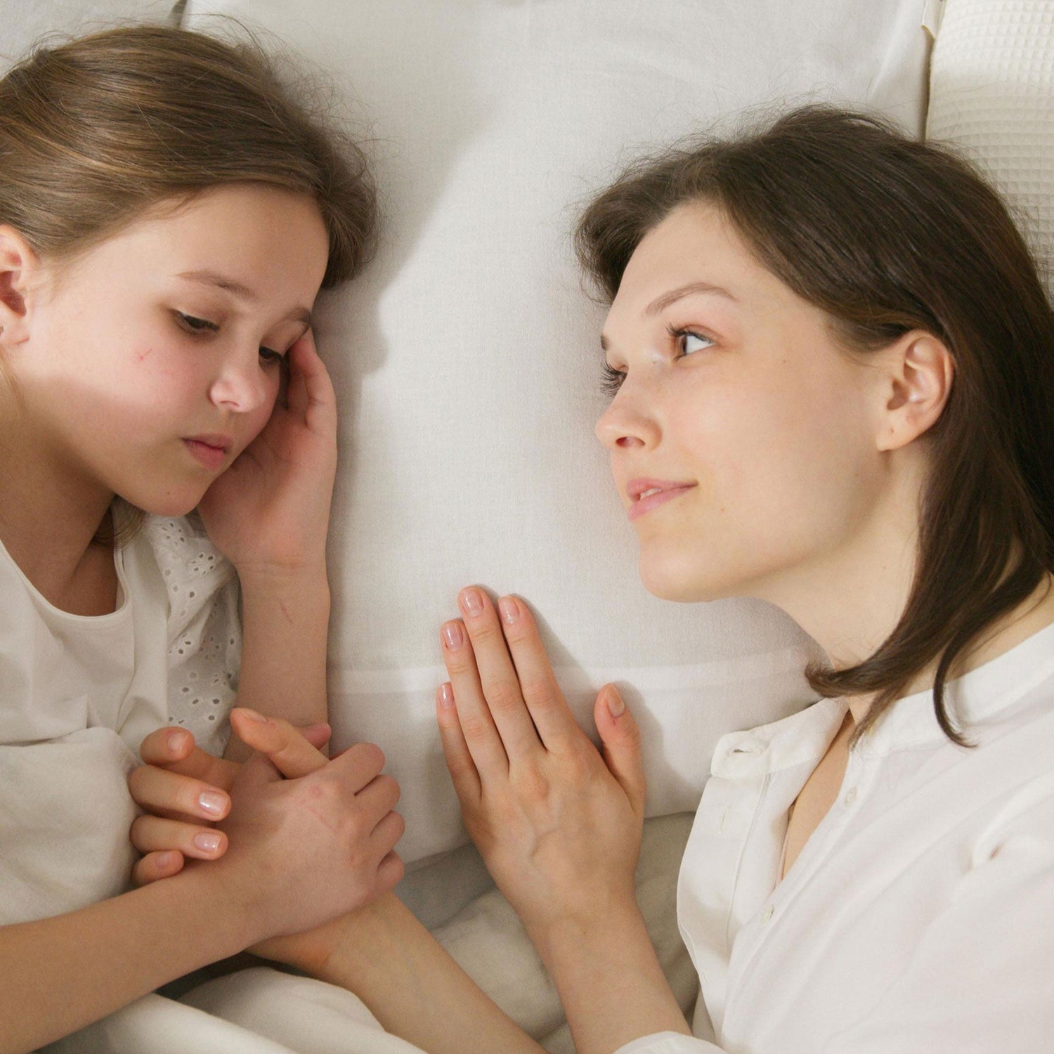 A mother consoling young daughter on bed after bed wetting